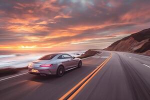 Prestige Luxury coupe cruising on coastal highway with the ocean stretching to the horizon and vibrant sunset sky photo
