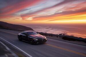 Prestige Luxury coupe cruising on coastal highway with the ocean stretching to the horizon and vibrant sunset sky photo