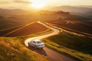 Prestige Full size sedan driving on winding countryside road with rolling hills and golden sunset light casting long shadows photo