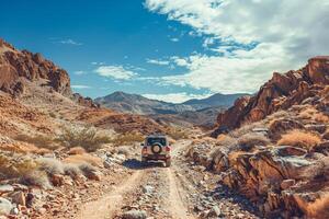 Compact SUV navigating rocky desert trail with towering mesas under a vast blue sky nature background photo