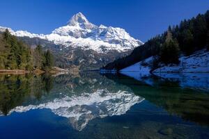 Majestic Snow Covered Mountain Peak Reflecting in Crystal Clear Alpine Lake Surrounded by Pine Forests   nature background photo
