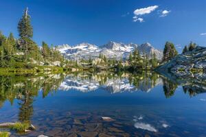 Pristine Alpine Lake Surrounded by Towering Pine Trees and Reflected Snow Capped Peaks   nature background photo