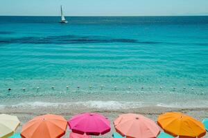beach umbrellas lining the shore with clear turquoise waters and a distant sailboat on the horizon nature background photo