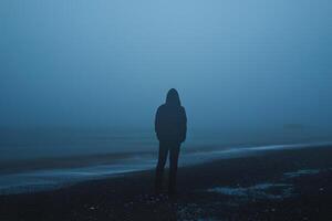 Hooded Figure Alone on Misty Beach at Dawn Mysterious and Atmospheric Coastal photo