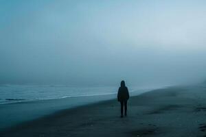 Hooded Figure Alone on Misty Beach at Dawn Mysterious and Atmospheric Coastal photo