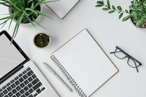 Laptop Mockup with Open Notebook on White Desk and  Writing Materials photo