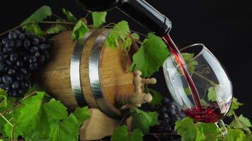 Wine. Red wine pouring from the bottle. Wine splashing into a wineglass. Ripe grapes with green leaves and oak barrel for wine on background video