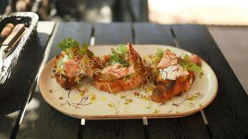 Fresh avocado toast with smoked salmon and poached eggs with grilled vegetables on plate on wooden table in city cafe. Healthy food and lifestyle. video