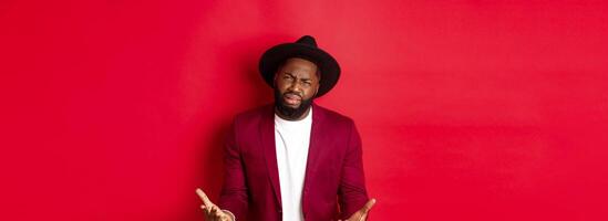 Frustrated and miserable african american man whining, complaining on life and crying, begging for something, standing over red background photo
