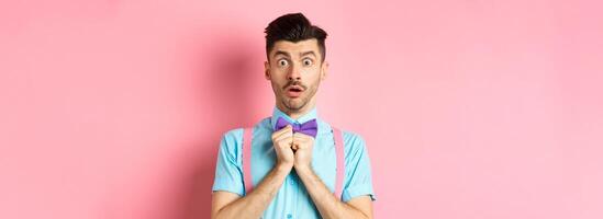 Startled and worried classy man in moustache, gasping and holding breath shocked, standing oin bow-tie over pink background photo