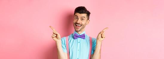 Handsome funny guy pointing fingers aside, showing left and right logo and smiling, recommending two choices, standing on pink background photo