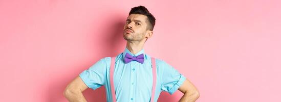 Proud and confident caucasian guy with moustache and bow-tie, looking arrogant with chin up, frowning and looking at camera, standing on pink background photo