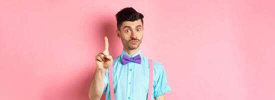 Young funny guy showing finger to explain something, prohibit or warn you, standing on pink background photo