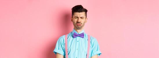 Sad and lonely man crying on valentines day, feeling lonely without lover, standing over pink background photo
