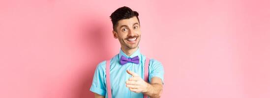 Nice to meet you. Handsome young man stretch out hand for handshake, smiling friendly and polite, introduce himself, standing over pink background photo
