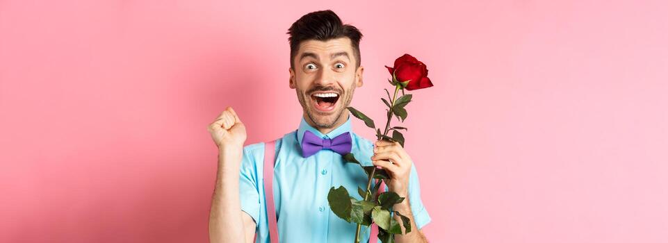san valentin día y romance concepto. emocionado novio saltando desde felicidad en romántico fecha, participación rojo Rosa y celebrando, en pie en rosado antecedentes foto