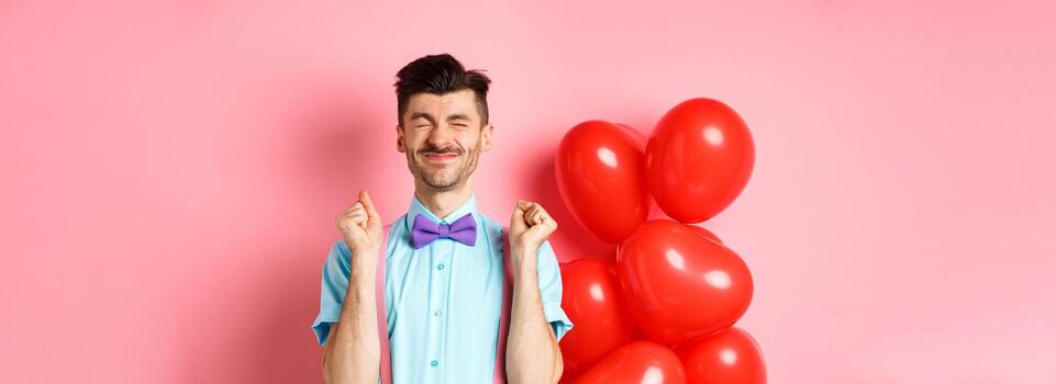 san valentin día concepto. alegre chico saltando desde emoción antes de romántico fecha, en pie cerca grande rojo corazones globos y celebrando, rosado antecedentes foto
