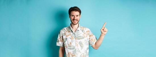 Smiling tourist in hawaiian shirt pointing finger at empty space, showing logo. Concept of vacation and travelling photo