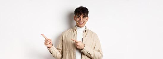 Handsome caucasian man in glasses smiling, pointing fingers at upper right corner, showing logo on white background photo