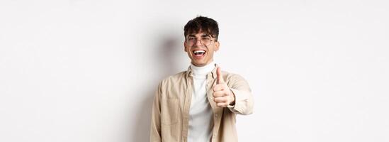 Nice one. Happy young man laughing and showing thumb up, like something good, standing on white background, complimenting you photo