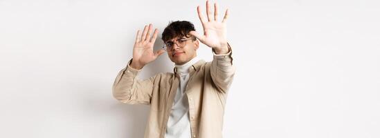 Image of reluctant and annoyed man raising hands up to block offer, refusing and asking to stop, telling no, declining something, standing on white background photo
