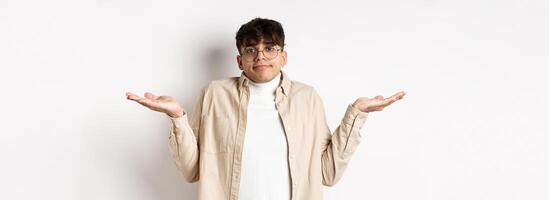 Portrait of handsome young man looking confused, know nothing, shrugging shoulders and spread hands sideways clueless, standing on white background photo