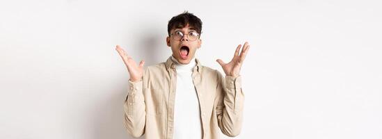 Scared young man in panic, screaming and looking axious, jumping startled and shocked, shaking hands nervously, standing on white background photo