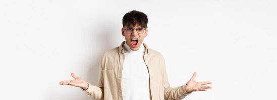 Portrait of angry frustrated man shouting and having argument, spread hands sideways and grimacing outrated, standing pissed-off on white background photo