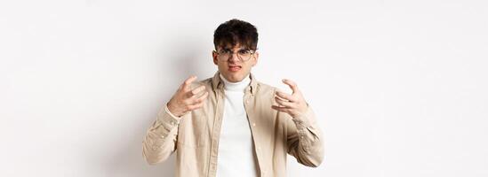 Portrait of annoyed and mad guy wants to strangle someone, grimacing from hatred and clench arms, standing bothered on white background photo