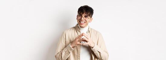 Portrait of hipster guy in glasses with white smile, steeple fingers as having plan, scheming something interesting, standing cunning on white background photo