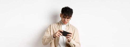 Portrait of handsome young man playing game on mobile phone, tilt smartphone to play racing, standing on white background photo