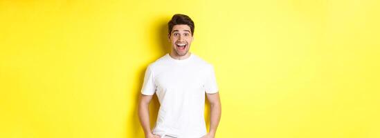 Man looking surprised, smiling amazed and looking at announcement, standing near copy space, yellow background photo