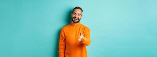 Friendly nice guy extend hand for handshake, greeting you and smiling, saying hello, standing over light blue background photo
