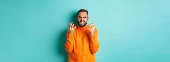 Image of angry man looking disappointed and mad, shaking hands and grimacing with disdain, standing distressed against light blue background photo
