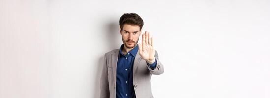 Hold right there. Serious businessman in suit stretch out hand and tell to stop, frowning and look confident, disapprove action, prohibit something bad, standing on white background photo