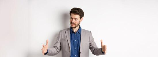 Excited handsome businessman showing long size thing, big object with stretch out hands, standing in suit on white background photo