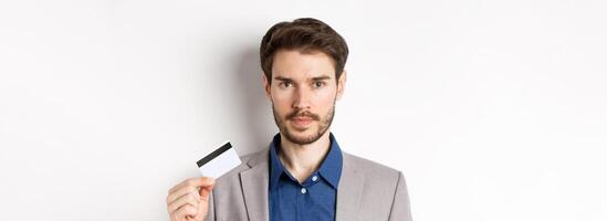 Finance. Close up of handsome bearded businessman in suit showing plastic credit card, standing serious on white background photo