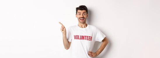 Happy smiling volunteer pointing finger left at copy space, showing announcement, white background photo