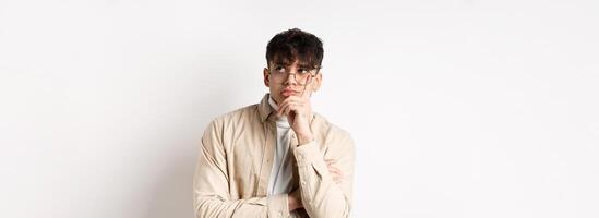 Sad and lonely young man looking at empty space with distressed face, standing thoughtful on white background photo
