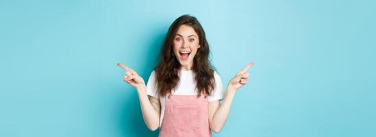 Pick your side. Smiling excited woman screaming of joy, pointing fingers sideways at left and right copy space, showing advertisement good deal, standing against blue background photo