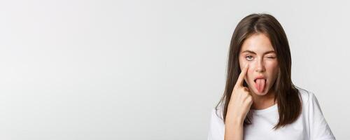 Close-up of silly attractive young girl showing tongue and pulling eyelid, watching you photo