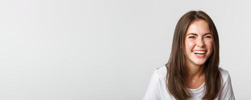 Close-up of happy and carefree brunette girl smiling and laughing from joy, standing white background photo