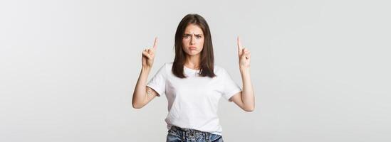 Sulking timid girl pointing fingers up, feeling upset photo