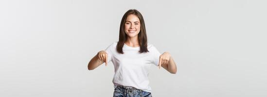 Satisfied smiling brunette girl pointing fingers down, recommend product photo