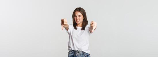 Disgusted brunette girl grimacing from dislike and showing thumbs-down photo