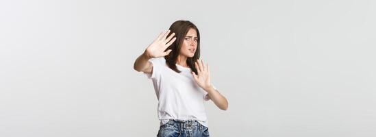 Scared and insecure cute girl raising hands in stop gesture, defending herself photo