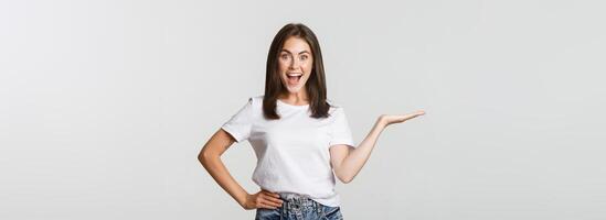 Excited beautiful girl extend arm, holding something on hand and looking happy photo