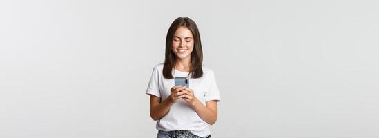Smiling attractive girl using mobile phone and looking at screen pleased photo