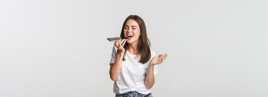 Friendly attractive brunette girl talking on speaker, record voice message at smartphone, white background photo