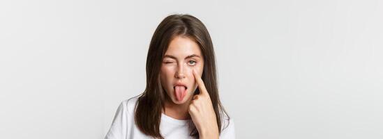 Close-up of silly attractive young girl showing tongue and pulling eyelid, watching you photo